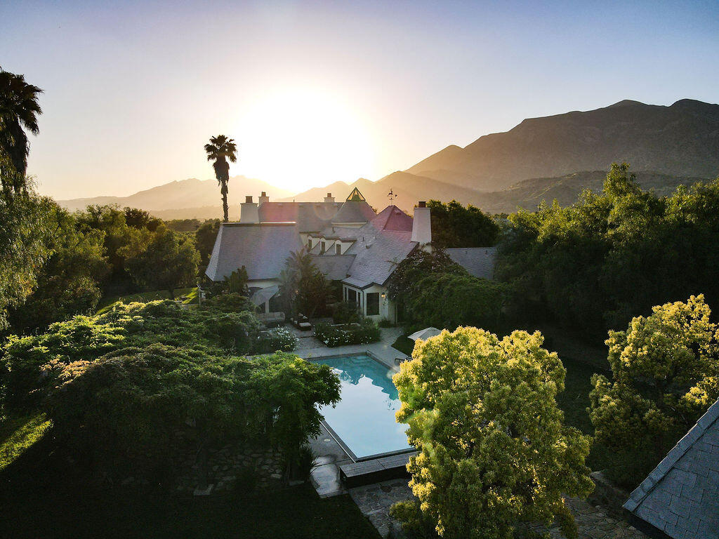 Arial view of estate and pool surrounded by trees and mountains